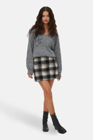 Korte rok met ruitpatroon van Vero Moda, gecombineerd met een grijze trui en zwarte laarzen.
