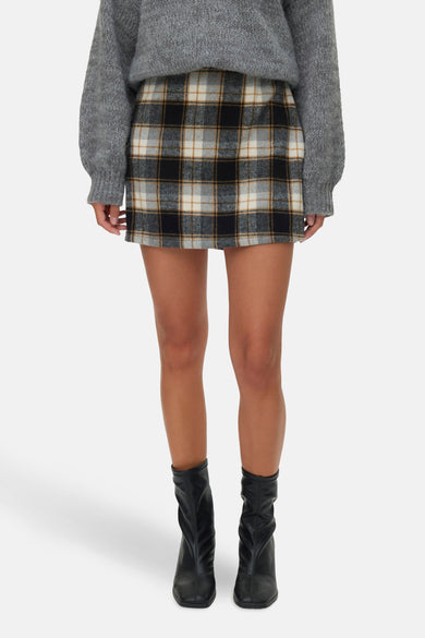 Multikleurige korte rok van VERO MODA, met ruitpatroon, gecombineerd met een grijze trui en zwarte laarzen.
