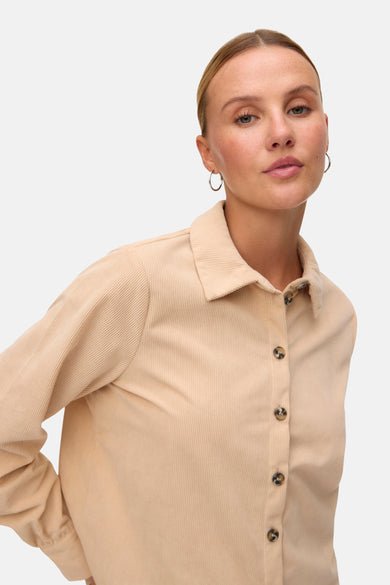 Chemise beige de VERO MODA avec fermeture à boutons et texture corduroy, portée avec des boucles d'oreilles en argent.