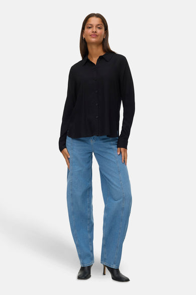 Zwart hemd met lange mouwen van VERO MODA, gedragen met blauwe jeans met hoge taille en zwarte laarzen.