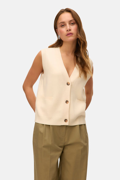 Beige gilet van VERO MODA, met knoopsluiting, zakken en gedragen over een olijfgroene pantalon.
