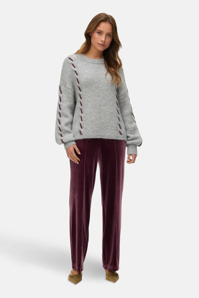 Sweat gris à col rond de Vero Moda, avec des broderies décoratives sur les manches, associé à un pantalon en velours et à des chaussures à lacets.