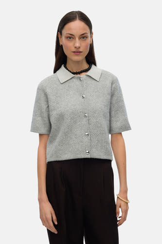Grijs gilet van VERO MODA, met korte mouwen, zilveren knopen en gedragen met een zwarte parelketting.
