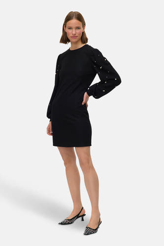 Zwarte jurk met lange mouwen van Vero Moda, versierd met parels op de mouwen, gecombineerd met zwarte schoenen.
