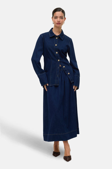 Lange donkerblauwe denim rok van VERO MODA met goudkleurige knopen, gecombineerd met een bijpassend denim overhemd.
