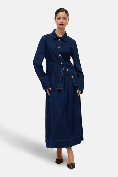 Lange donkerblauwe denim rok van VERO MODA met goudkleurige knopen, gecombineerd met een bijpassend denim overhemd.
