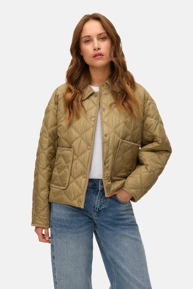 Manteau vert, court de Vero Moda avec un motif à carreaux et des poches, porté sur un T-shirt blanc et des jeans bleus.