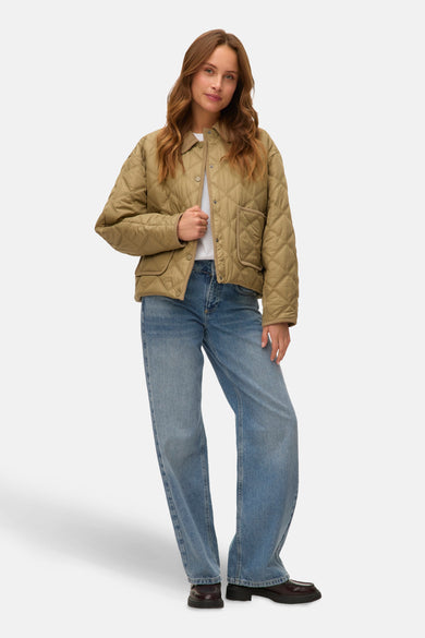 Manteau court vert de VERO MODA, avec un motif à carreaux et porté avec une chemise blanche et un jean bleu.