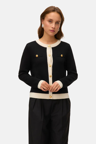 Gilet noir de VERO MODA, avec des accents crème et des boutons dorés, porté avec un pantalon noir.
