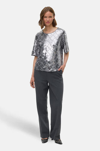 Zilveren blouse met korte mouwen van VERO MODA, met pailletten en een ruitpatroon, gecombineerd met grijze pantalon.