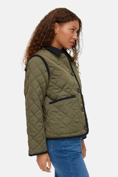 Groene korte jas van Vero Moda, met diamantstiksel en zwarte afwerking, gedragen met een blauwe jeans.
