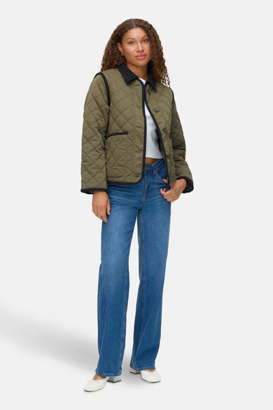 Groene korte jas van VERO MODA, met diamantstiksel en gedragen met een wit shirt en blauwe jeans.
