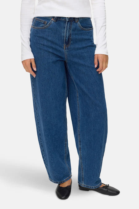 Jean en denim bleu de VERO MODA, avec des jambes larges et une taille haute, porté avec un t-shirt blanc et des chaussures noires.