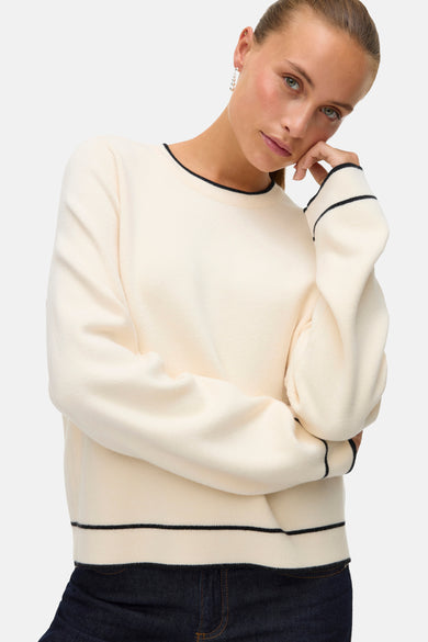 Ecru trui met ronde hals van VERO MODA, met zwarte bies langs de halslijn, manchetten en zoom, gedragen met donkere jeans.
