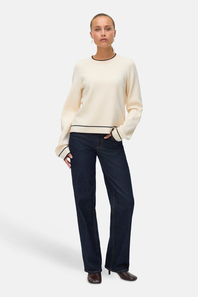 Ecru trui met ronde hals van VERO MODA, afgewerkt met zwarte details, gecombineerd met donkere jeans en bruine schoenen.
