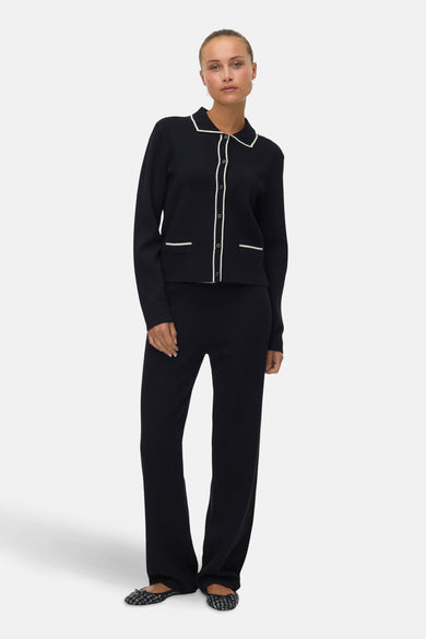 Zwart gilet van VERO MODA, met witte biezen en bijpassende zwarte broek en platte schoenen.
