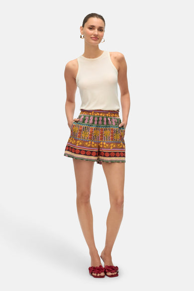 Multikleurige short van VERO MODA®, met een patroon van tropische planten en schelpen, gecombineerd met een witte top en rode slippers.
