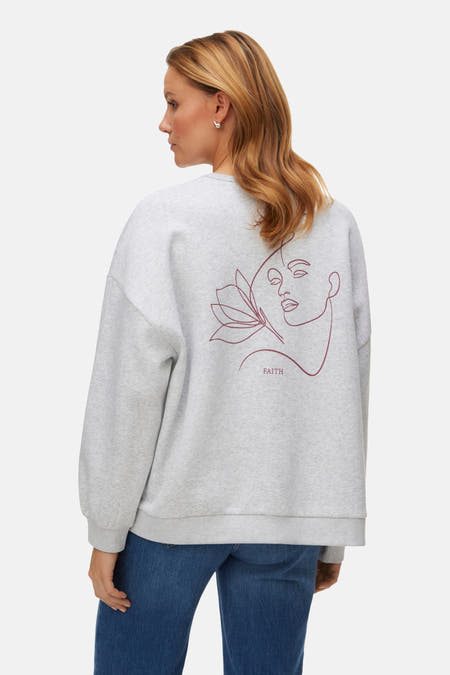 Grijze sweater van VERO MODA® met grafische print op de rug, gecombineerd met blauwe jeans.
