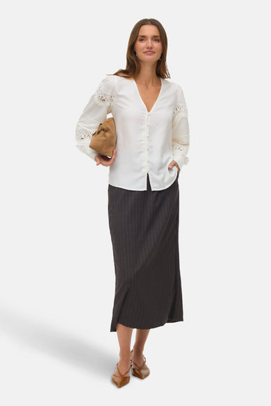 Wit langmouw overhemd van VERO MODA, met kanten details op de mouwen, gecombineerd met een gestreepte rok en bruine hakken.