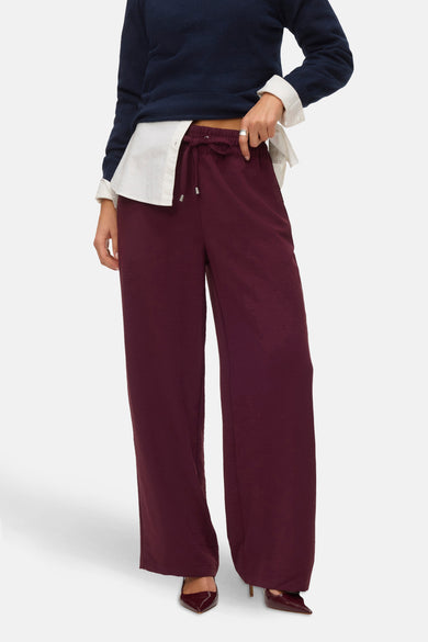 Pantalon Bordeaux de VERO MODA, avec des jambes larges et associé à une blouse blanche et des chaussures coordonnées.