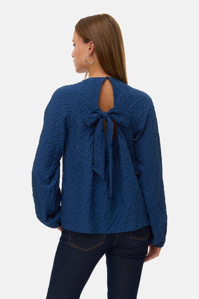 Chemisier bleu à manches longues de Vero Moda, avec une texture subtile et combiné avec un jean foncé et des bottes noires.