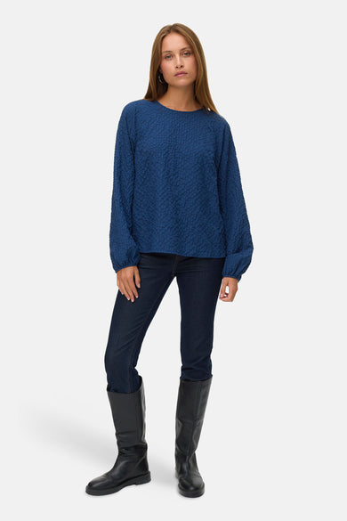 Blauwe blouse met lange mouwen van Vero Moda, met een subtiele textuur en gecombineerd met donkere jeans en zwarte laarzen.
