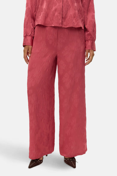Roze broek van VERO MODA®, met een all-over bloemenpatroon, gecombineerd met een roze blouse en bruine schoenen.
