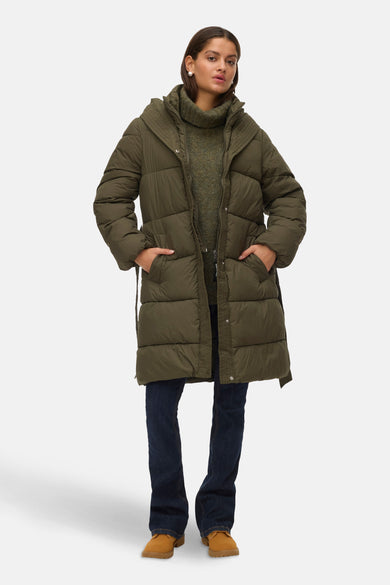 Groene lange jas van Vero Moda met capuchon, gedragen over een groene trui en donkere jeans.