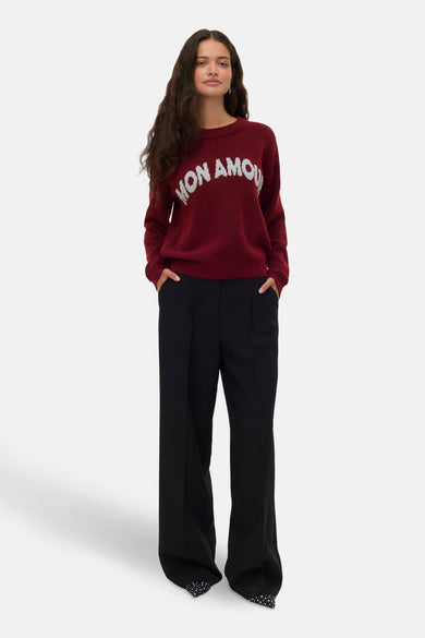 Pull rouge à col rond de VERO MODA, avec le texte blanc "Mon Amour", associé à un pantalon noir et des chaussures pointues.