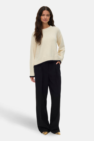Ecru trui met ronde hals van VERO MODA, afgewerkt met donkere details en gecombineerd met een zwarte pantalon.

