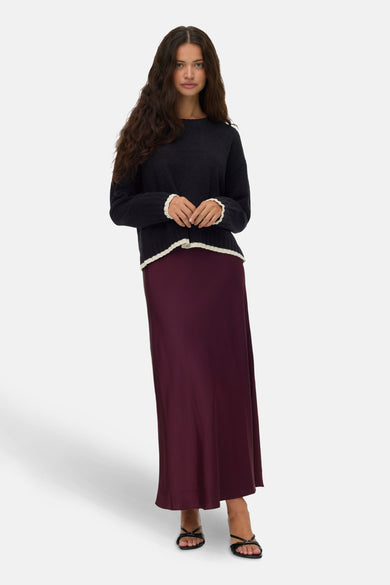 Zwarte trui met ronde hals van VERO MODA®, afgewerkt met geribbelde details bij de mouwen en zoom, gecombineerd met een lange bordeauxrode rok en zwarte sandalen.