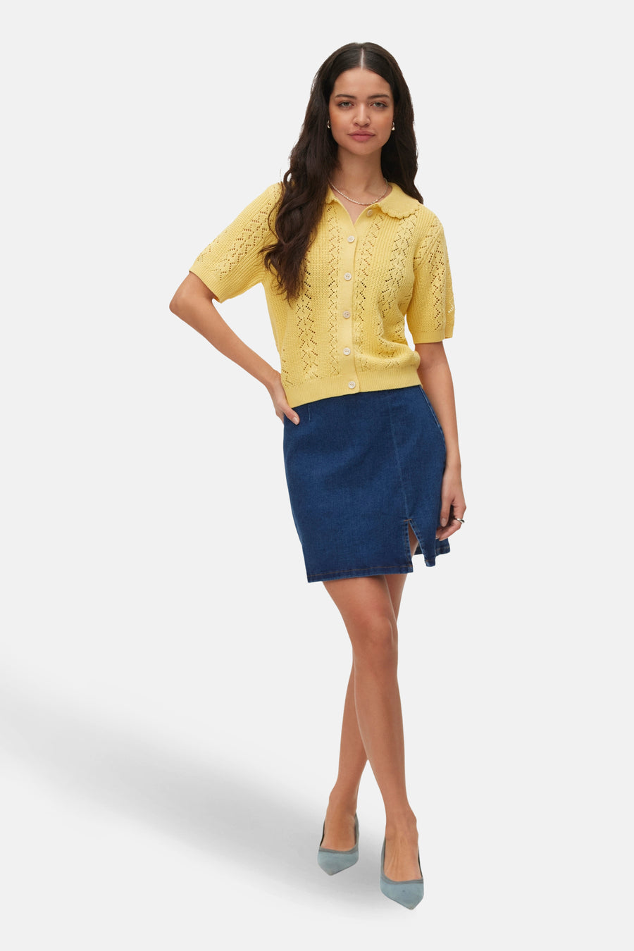 Geel gilet van Vero Moda, met korte mouwen en een knoopsluiting, gecombineerd met een donkerblauwe denim rok en blauwe pumps.
