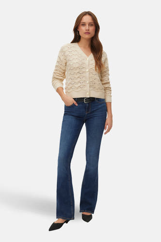 Ecru vest van VERO MODA, met knoopsluiting en een ajour gebreid patroon, gecombineerd met donkere jeans en zwarte schoenen.
