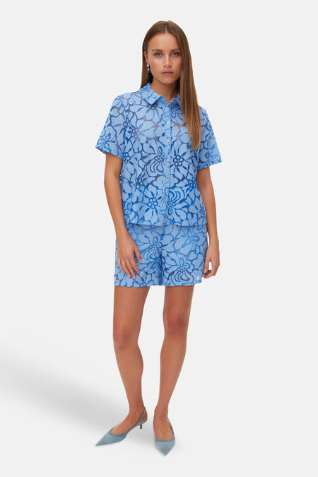 Blauw hemd met korte mouwen van VERO MODA® met bloemenkantpatroon, gedragen met bijpassende shorts en lichtblauwe hakken.