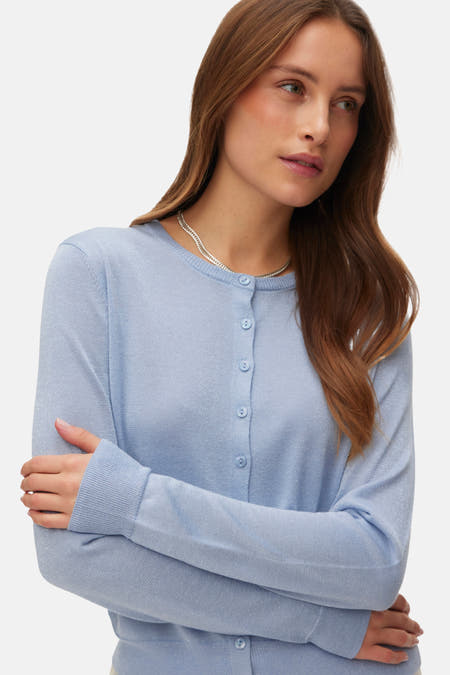Blauwe cardigan van VERO MODA, met lange mouwen en knoopsluiting, gedragen met een zilveren ketting.

