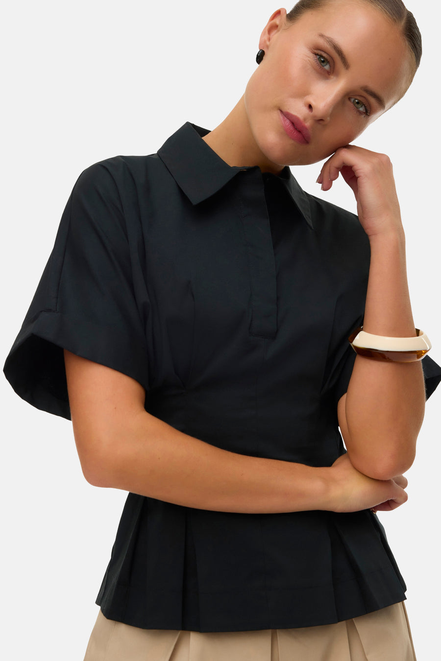 Chemisier noir à manches courtes de VERO MODA, avec peplum plissé, combiné avec une jupe beige et des chaussures noires.