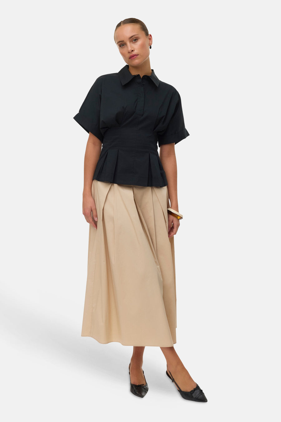 Zwarte blouse met korte mouwen van VERO MODA, met plissé peplum, gecombineerd met een beige rok en zwarte schoenen.