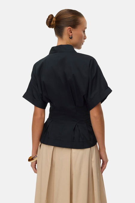 Zwarte blouse met korte omgeslagen mouwen van VERO MODA® met geplooide peplum taille, achterkant op model met beige plooirok.