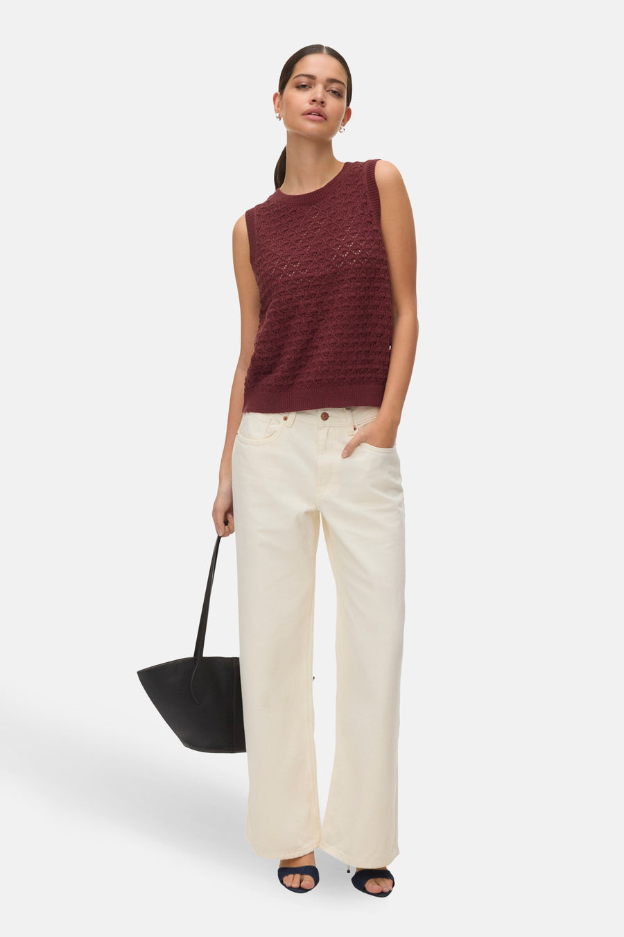 Baksteenkleurige debardeur van VERO MODA, met een open gebreid patroon, gecombineerd met crèmekleurige broeken en een zwarte handtas.