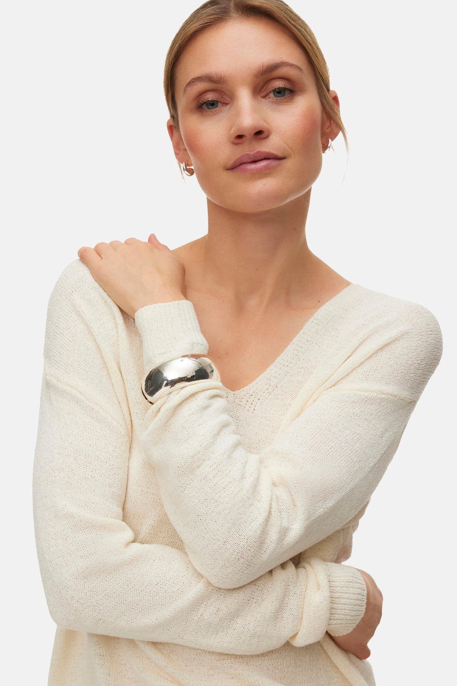 Pull col V écru de VERO MODA®, porté avec un pantalon large marron et des talons marron.