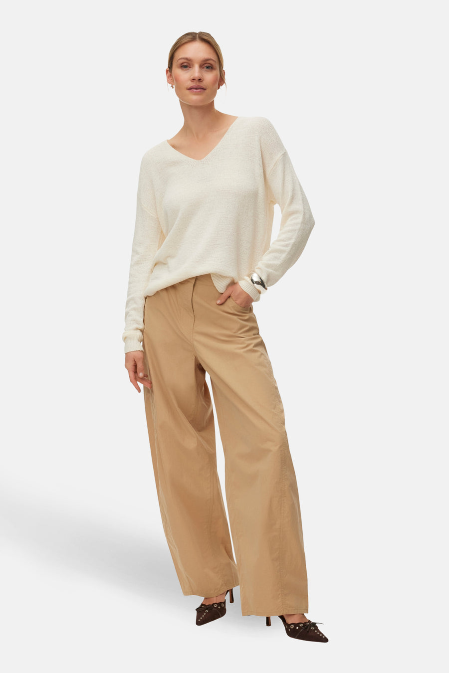 Ecru V-hals trui van VERO MODA®, gedragen met wijde, bruine broek en bruine hakken.
