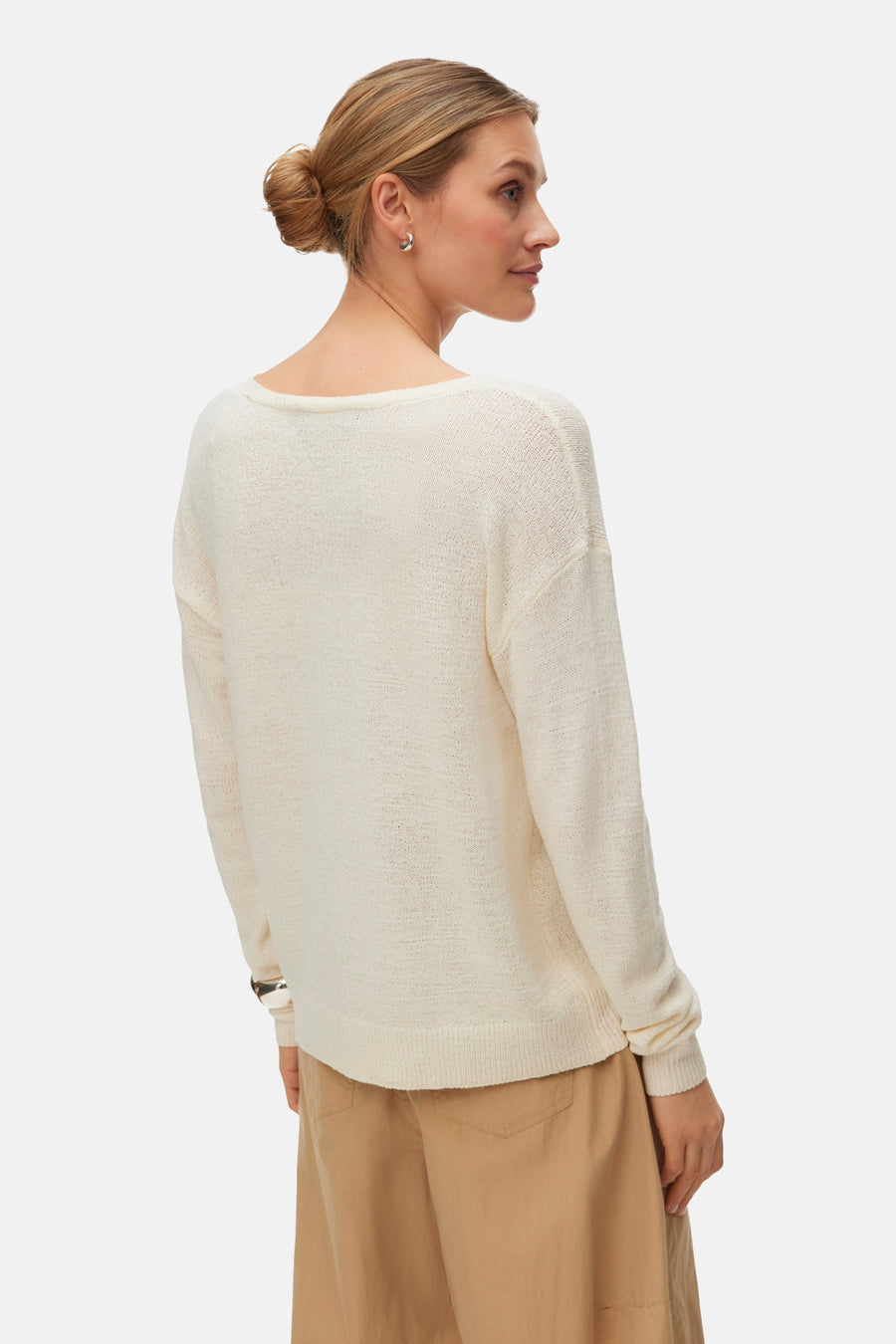 Pull écru à col en V de Vero Moda, à manches longues, porté avec un pantalon marron et des boucles d'oreilles argentées, vue arrière.