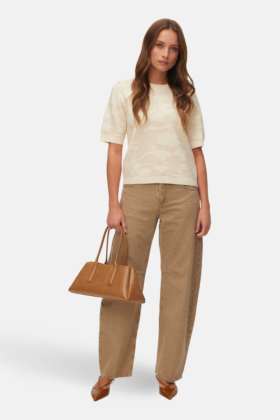 Ecru trui met ronde hals van VERO MODA, met een subtiel bloemdessin, gecombineerd met bruine jeans en leren handtas.
