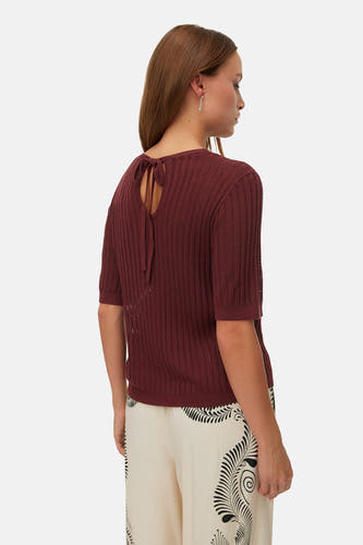 Pull marron à col rond de VERO MODA, avec un dos noué et une texture côtelée, porté avec un pantalon à motif.