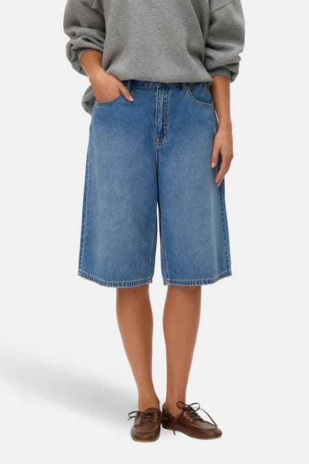 Korte middenblauwe denim short van VERO MODA, met losse pasvorm en bruine schoenen.
