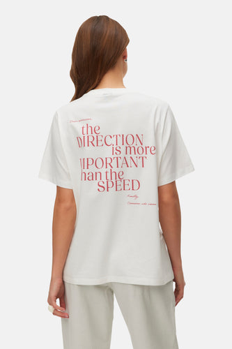 Achterkant van een vrouw met een witte T-shirt met rode tekst, lichtgrijze broek.