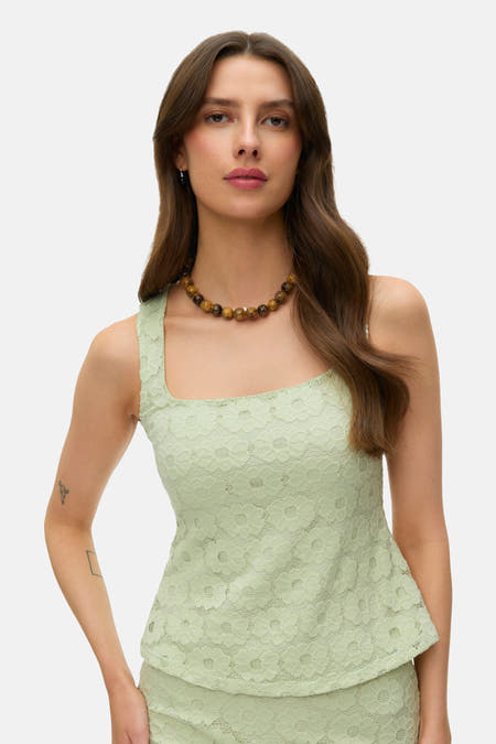 Mouwloze groene blouse van VERO MODA met kantpatroon, vierkante halslijn en peplumzoom, gedragen met een kralenketting.