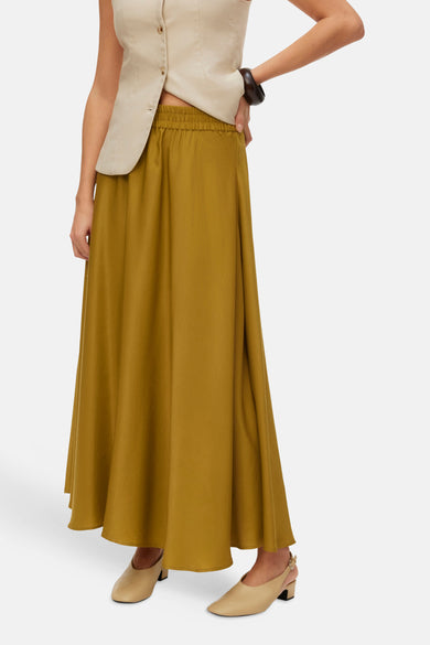 Jupe longue verte de VERO MODA®, portée avec un gilet beige sans manches et des chaussures claires.