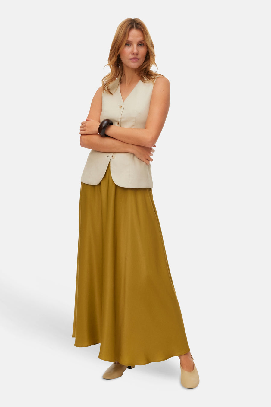 Lange groene rok van VERO MODA®, gedragen met een beige mouwloos vest en lichte schoenen.