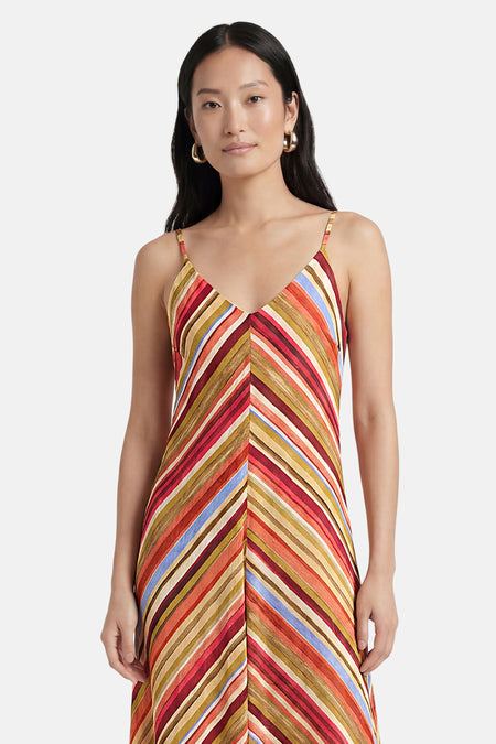 Robe sans manches à rayures diagonales multicolores de VERO MODA® avec fines bretelles et col en V, porté par un mannequin avec des créoles dorées.